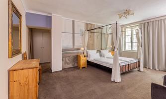 An elegant bedroom with a four-poster bed and beautiful decor. Large windows provide plenty of daylight and an inviting atmosphere.