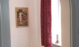 A bright room with a green carpet and a window. In front of the window hangs a red curtain, and on the wall, there is a picture.