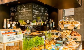 An inviting buffet with fresh rolls, healthy snacks, and a wide selection of dishes. Handwritten menus and illustrations can be seen on the wall.