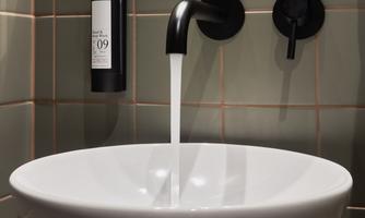 A modern sink with a round bowl and black faucet. In the background, green glasses are visible.