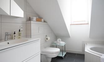 A modern bathroom with sloping walls and minimalist design. It includes a sink, a toilet, and a bathtub.