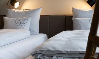 A modernly furnished bedroom with two single beds. The walls are in neutral colors, and there is cozy lighting.
