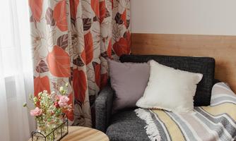 A cozy corner in a room with a black armchair, a small table, and a colorful curtain. On the table are flowers and a blanket is laid over the armchair.