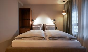 A modern bedroom with a large, comfortable bed and soft lighting. The windows are decorated with curtains, and the room feels inviting and cozy.