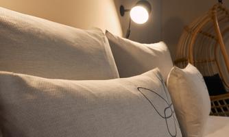 A cozy bedroom with soft pillows and gentle light. In the background, a decorative chair can be seen.