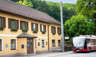 A yellow house with many windows and green plants. A city bus is at the stop in front of the building.
