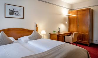 A cozy bedroom with a large double bed and soft colors. A simple wooden dresser and a desk complete the furnishings.
