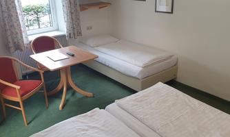 A simple room with two single beds and a table. The window offers a view of the outdoors.