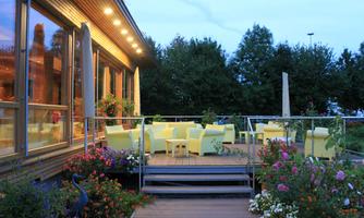 A cozy terrace surrounded by bright furniture and blooming plants. The evening sky is clear, and the space feels inviting.
