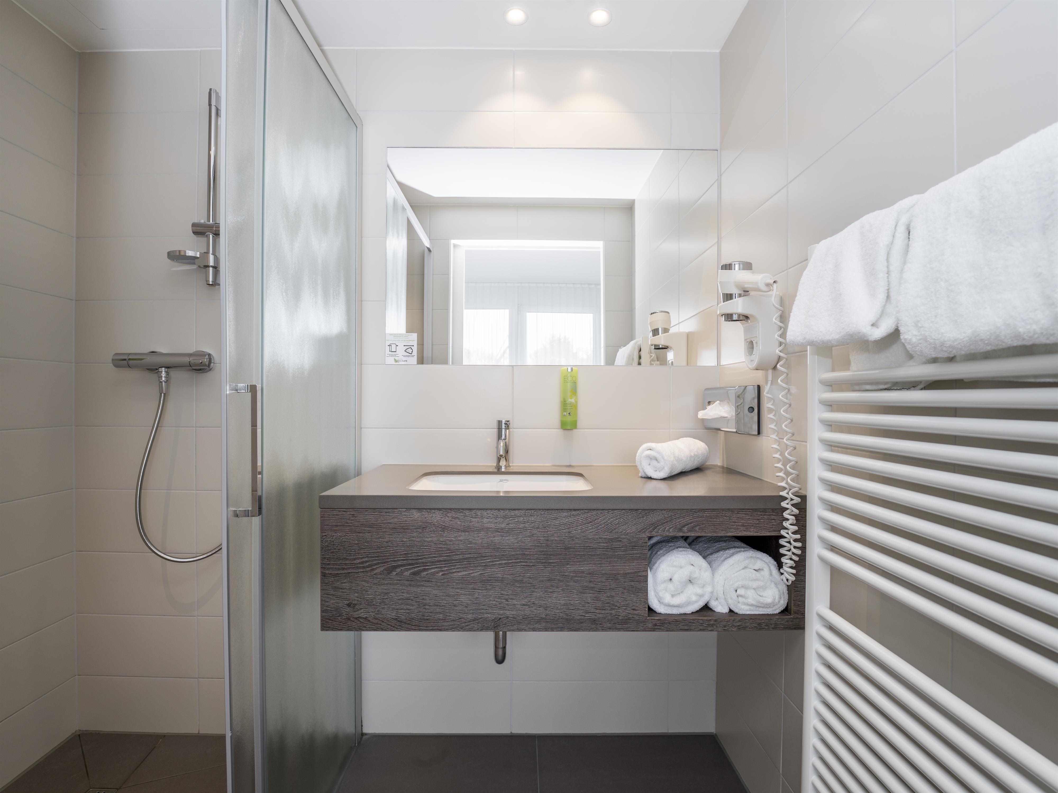 A modern bathroom with a shower and a wooden sink. Towels and a towel warmer are also available.