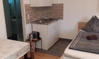 A cozy room with a single bed and a small kitchenette. The table is covered with a tablecloth and there is a warm atmosphere.