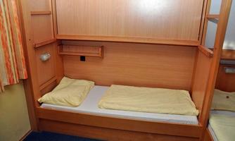 A simple sleeping nook with wooden walls and a bed. The bedding is bright and neatly arranged on the sleeping area.