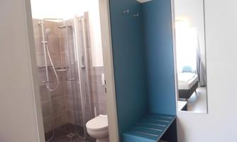 A modern bathroom with a shower and a toilet. An entrance area is also visible with a blue seating area and a mirror.