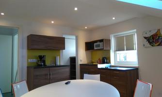 A modern kitchen with wooden cabinets and light walls. A large round table with white chairs is in the room.