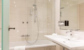 A modern bathroom with a bathtub and a shower. The walls are brightly tiled, and there is a large mirror above the sink.