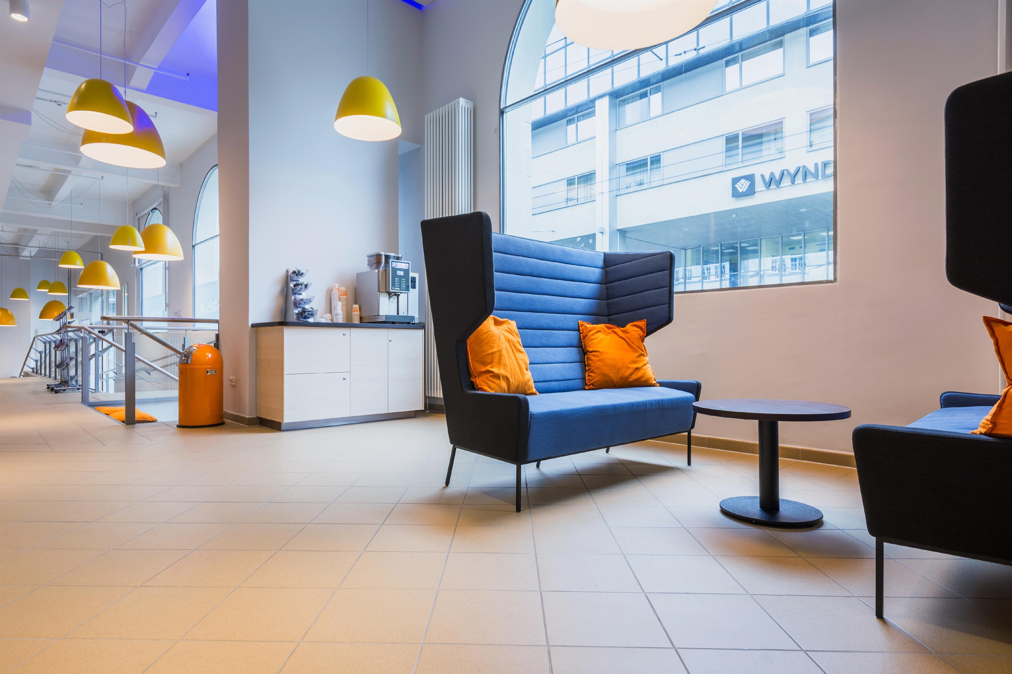 A modern lounge area with comfortable seating and bright ceiling lights. Large windows provide plenty of daylight and an open view outside.