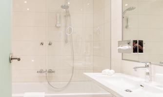 A modern bathroom with a bathtub and a shower. The walls are painted in light colors, and there is a large mirror.