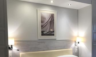 A modern bedroom with a comfortable double bed and soft lighting. A painting hangs on the wall, and there are bedside lamps.
