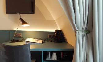 A modern workspace in a cozy room. The desk is equipped with a lamp, a TV, and a coffee maker.