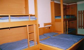 A simple room with two bunk beds and blue checkered bedding. The walls are light and the furniture is made of wood.
