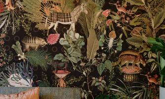 A cozy seating area with a sofa and decorative cushions. The wall is adorned with a colorful plant pattern and a simple lamp hangs from the ceiling.