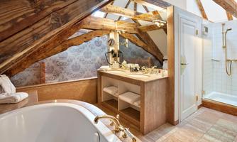 A modern bathroom in the attic with wooden beams. It features a bathtub, a sink, and a shower.