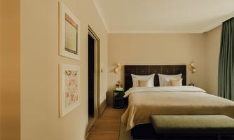 A modern bedroom with a large bed and stylish decorations. The walls are painted in soft colors and there is a window with curtains.
