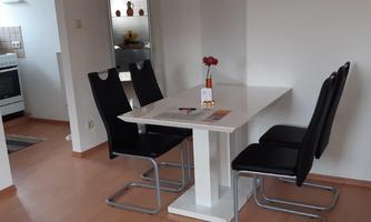 A modern dining table with four black chairs is located in a bright kitchen. There is a small flower vase on the table.