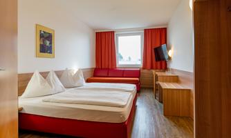 A modern bedroom with two beds and a red sofa. Large windows and cozy wooden furniture create a pleasant atmosphere.