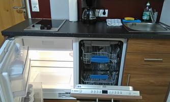 A modern kitchen with refrigerator and dishwasher. The countertop is neatly equipped with a coffee machine and a draining board.