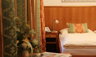 A cozy bedroom with a bed and colorful curtains. On the nightstand, there is a lamp and a telephone.