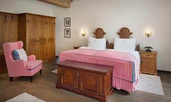 A bright bedroom with two single beds, wooden wardrobes, and a comfortable armchair. The decor is cozy and inviting.