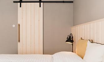 A modern bedroom with a wooden sliding door and a cozy bed. The walls are light and the decoration is simple and stylish.