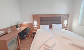 A modern bedroom with two single beds and a wooden desk. The walls are light and there is soft lighting on the nightstands.