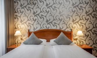 A cozy bedroom with a double bed and elegant wallpaper. Two bedside lamps provide warm light.