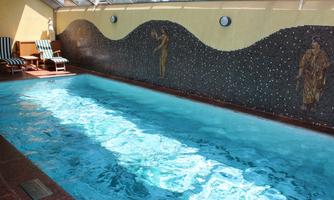 An elegant indoor pool with clear water and artistic wall design. There are loungers for relaxing next to the pool.