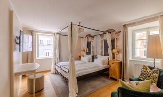 A cozy bedroom with a four-poster bed and soft colors. The room has large windows and an inviting atmosphere.