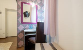 A cozy room with a desk and a chair. On the wall, there is a mirror and a television, surrounded by a decorative pattern.
