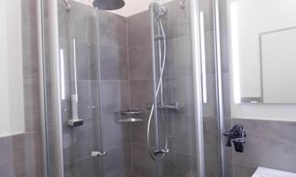 A modern shower with transparent glass doors and gray tiles. The lighting and fixtures are designed in a contemporary and elegant style.