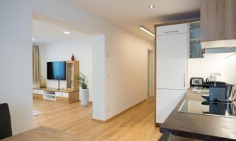 Modern apartment with an open kitchen and a bright living room. The floor is made of wood and there is a television and elegant furniture.