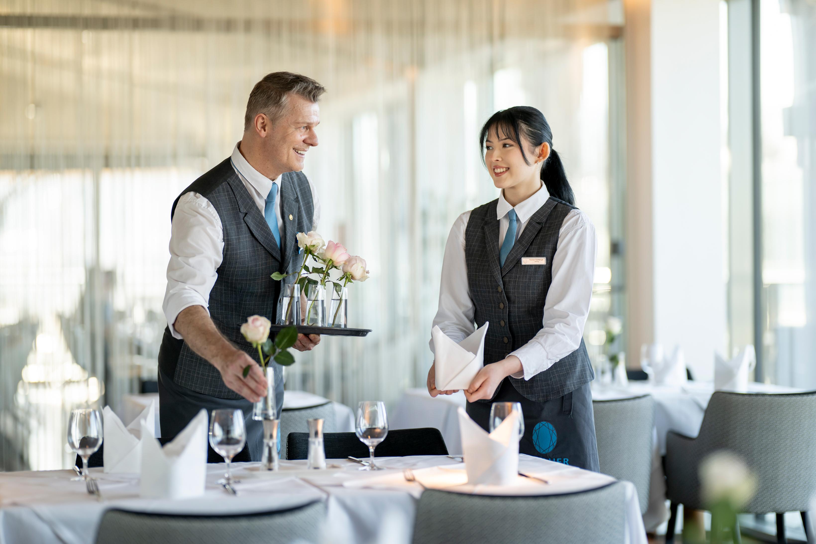 Two service staff are setting an elegant table in a restaurant. The atmosphere is friendly and inviting.
