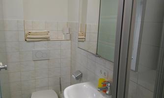 A modern bathroom with a bright tiled floor. There is a shower, a sink, and fresh towels.