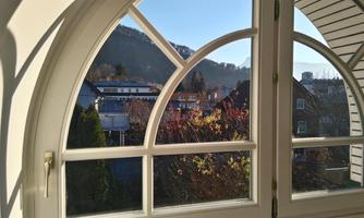 A view from a window with an architectural frame. In the background, mountains and houses can be seen, surrounded by colorful foliage.