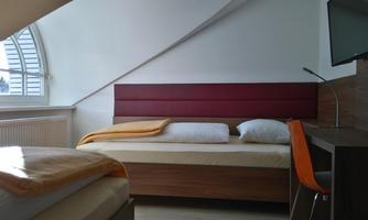 A modern bedroom with two beds and a desk. The room has an arched window and a bright, friendly atmosphere.
