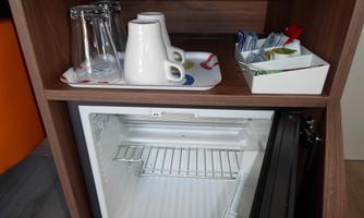 A refrigerator in a furniture cabinet with glasses, cups, and a selection of tea bags. Below it, the empty refrigerator is visible.