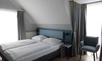 A modern bedroom with a double bed and a comfortable armchair. The atmosphere is bright and inviting, with curtains at the windows.