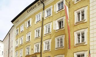 A charming hotel building with a yellow facade and several windows. The building is adorned with various national flags.