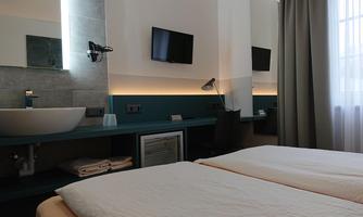 A modern hotel room with two beds, a desk, and a television. The room features a stylish bathroom with a sink and large windows.