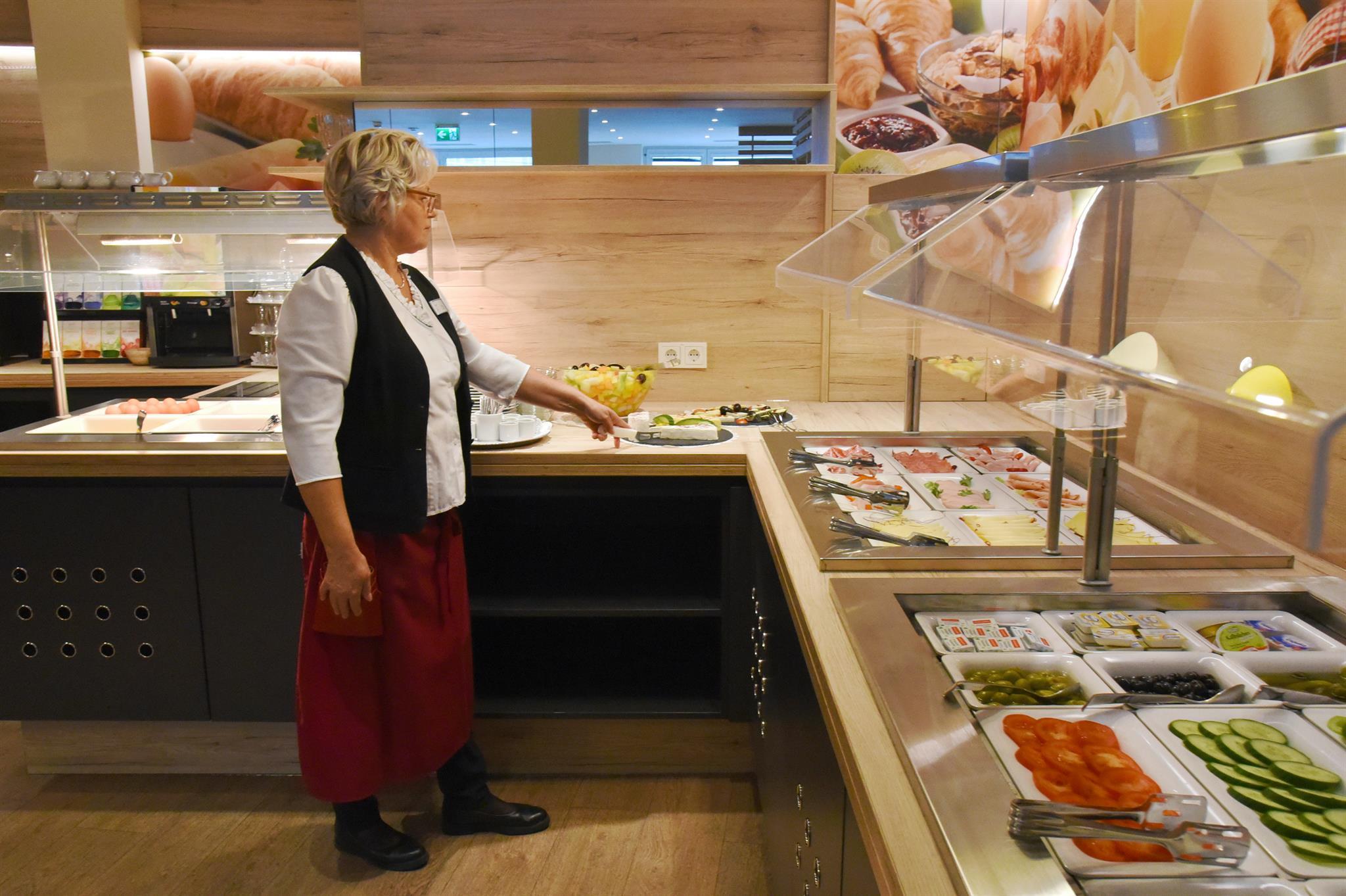 A woman is standing at a buffet with fresh ingredients. The counter is well-stocked with various salads and side dishes.
