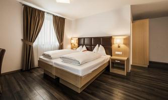 A modern bedroom with a double bed and wooden floor. The room has curtains and warm light for a cozy atmosphere.